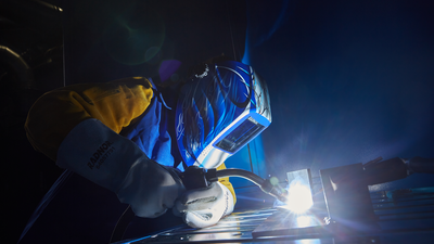 A well-equipped man is welding, wearing a visor and a mask