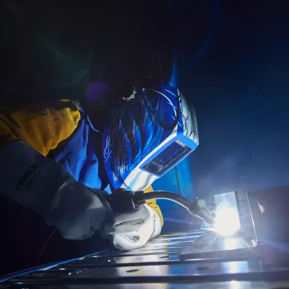 A well-equipped man is welding, wearing a visor and a mask